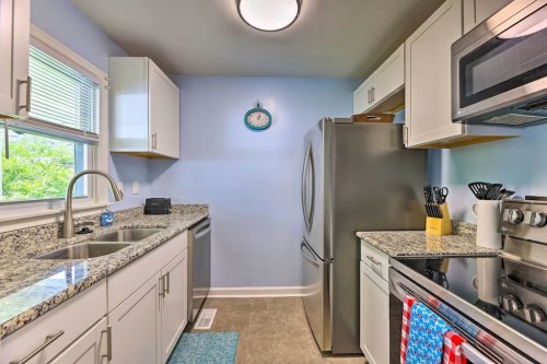 Bright kitchen with granite countertops, stainless steel appliances, and light blue walls. Features a window and clock.