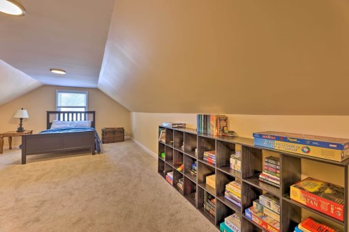 Cozy attic bedroom with a bed, a lamp, and a bookshelf filled with board games and books. Soft carpet and natural light.