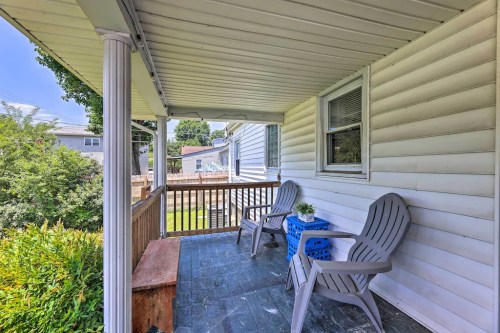 A cozy porch with two chairs and a small table, surrounded by greenery and a wooden railing.