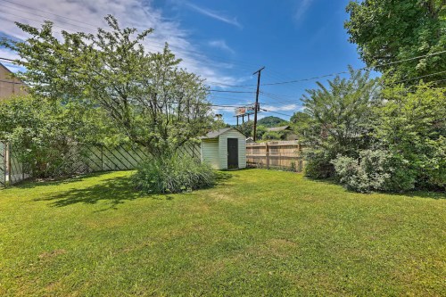 A grassy backyard with a small shed, surrounded by trees and shrubs under a blue sky with scattered clouds.