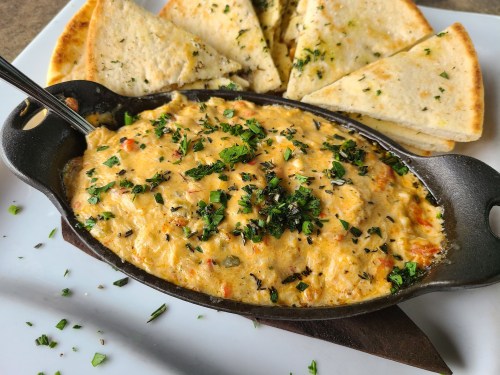 A skillet of creamy dip topped with herbs, served with toasted bread wedges on the side.