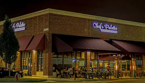 A restaurant exterior at night, featuring outdoor seating and a sign that reads "Chef's Palette."