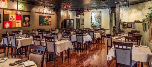 A spacious restaurant with wooden floors, neatly set tables, and colorful artwork on the walls.