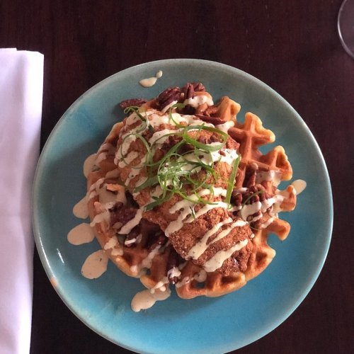 A plate of waffles topped with fried chicken, pecans, and drizzled with sauce, garnished with green onions.