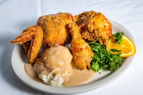 A plate of crispy fried chicken with mashed potatoes and gravy, garnished with parsley and an orange slice.