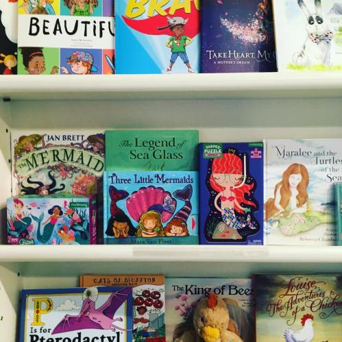 A colorful bookshelf filled with children's books, including titles about mermaids and sea adventures.