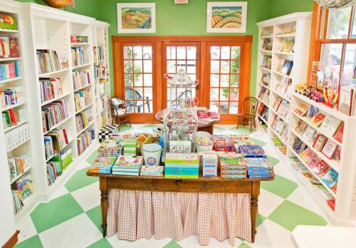 A cozy bookstore with shelves of books, a central table filled with games, and bright green walls.