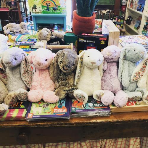 A row of plush bunnies in various colors, sitting on a table with children's puzzles and toys in the background.