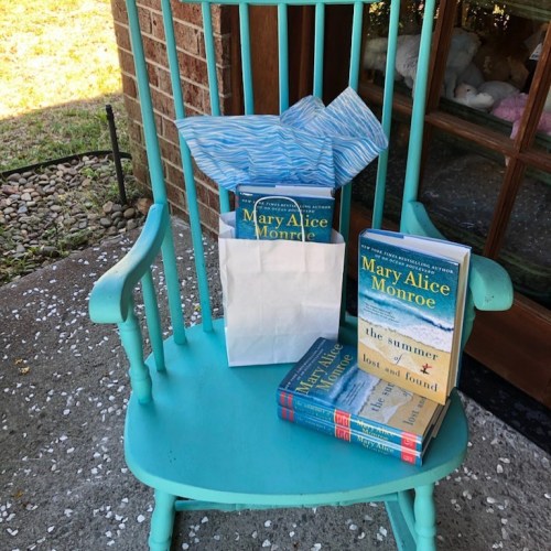 A turquoise rocking chair with a white gift bag and two books by Mary Alice Monroe on the seat.