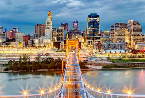 A vibrant city skyline at dusk, featuring a bridge illuminated with lights over a river.