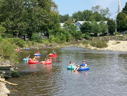 People floating on colorful inner tubes in a calm river surrounded by trees and a sunny sky.