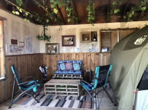 Cozy indoor space with a sofa, chairs, and a tent, decorated with plants and rustic wooden accents.