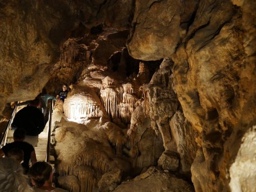 Visitors explore a dimly lit cave with impressive rock formations and a staircase leading deeper into the cavern.