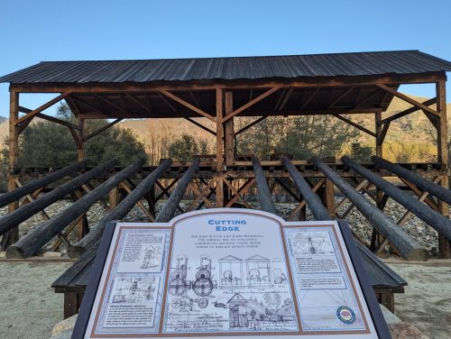 A wooden structure with a sign titled "Cutting Edge" detailing historical information, set against a clear blue sky.