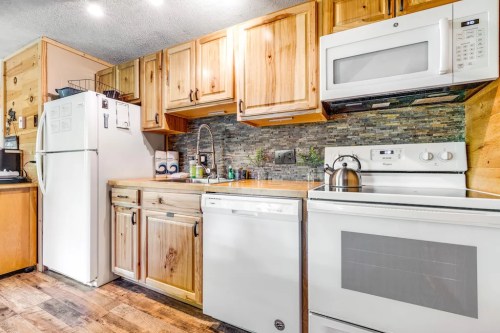 A cozy kitchen with wooden cabinets, a white refrigerator, and modern appliances against a stone backsplash.