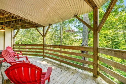 A wooden deck with red chairs overlooks a lush green forest, featuring trees and natural light.