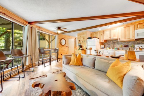 Cozy living space with a sofa, wooden coffee table, and kitchen, featuring large windows and warm wood accents.