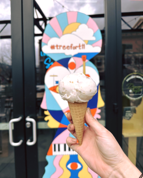 A hand holds an ice cream cone in front of a colorful mural featuring a face and musical elements.