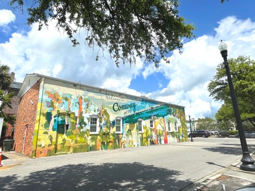 Colorful mural on a building in Conway, South Carolina, with blue skies and fluffy clouds above.