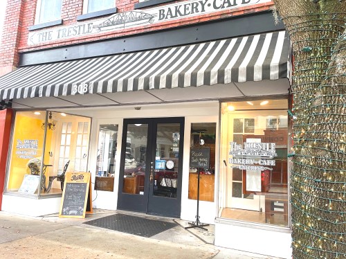 Exterior of The Trestle Bakery Cafe, featuring a striped awning, glass doors, and a chalkboard sign outside.