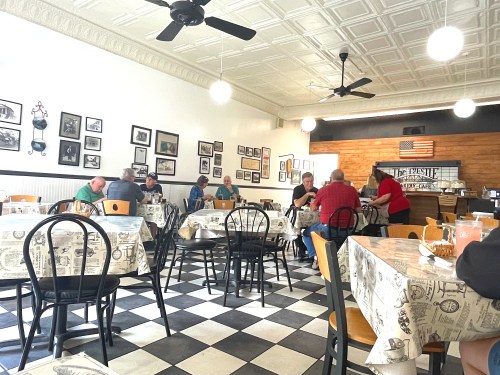 A cozy diner with checkered floors, tables set for dining, and patrons enjoying their meals and conversations.