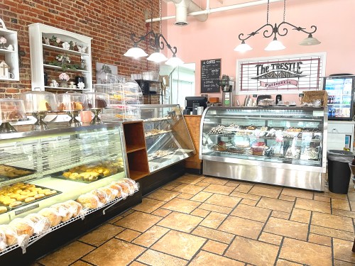 A cozy bakery interior with glass display cases filled with pastries and desserts, featuring brick walls and warm lighting.