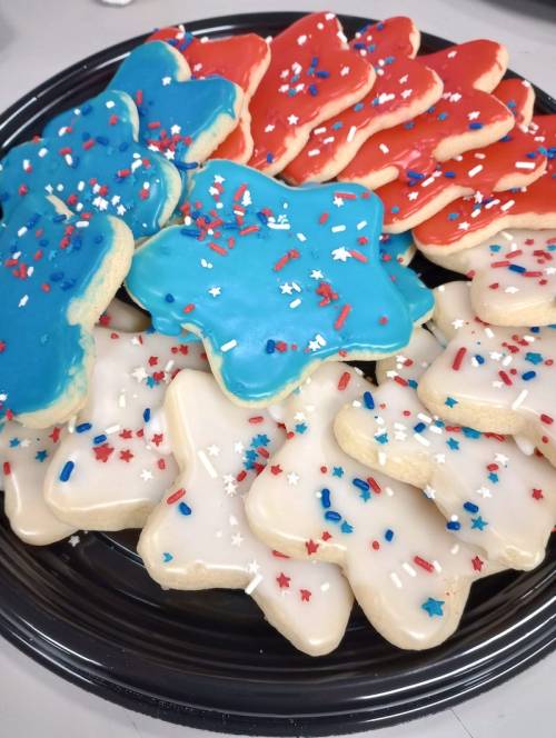 A black platter filled with star-shaped cookies decorated in red, white, and blue icing and festive sprinkles.
