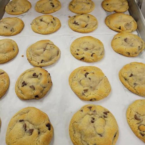 A tray of freshly baked chocolate chip cookies on parchment paper, golden brown and slightly chewy.