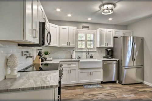 Modern kitchen with white cabinets, stainless steel appliances, a farmhouse sink, and wooden flooring. Bright and inviting space.