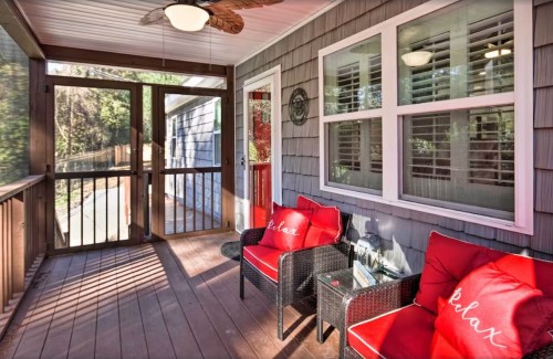 Cozy porch with red cushions on wicker chairs, a ceiling fan, and sunlight streaming through the windows.