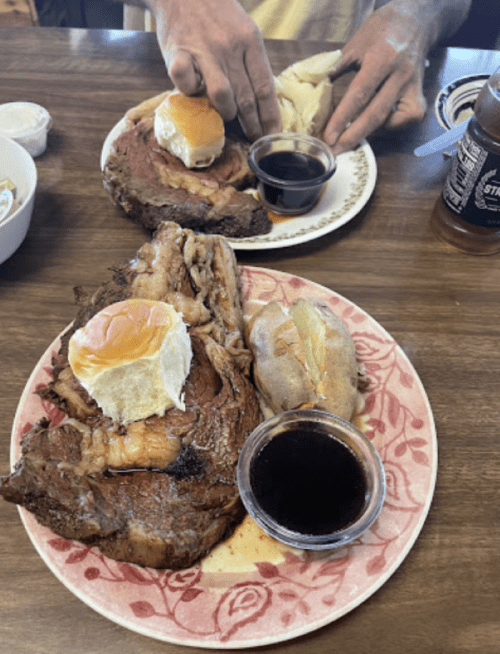 Two plates of food featuring slices of roast beef, rolls, and dipping sauce, with a side of baked potato.