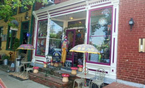 Colorful storefront with decorative umbrellas, small tables, and chairs outside, featuring vibrant window displays.
