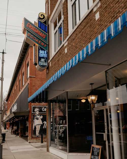 A street view of a brick building with a retro sign for "Crossroads Cookery" and blue-striped awnings.