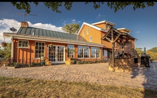 A charming orange farmhouse with a metal roof, surrounded by a stone patio and outdoor grill area.