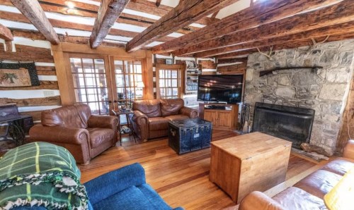 Cozy living room with wooden beams, leather sofas, a stone fireplace, and a wooden coffee table. Warm and inviting atmosphere.