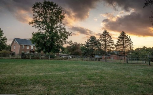 A serene landscape featuring a house, trees, and a grassy field under a colorful sunset sky.