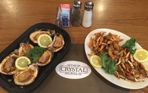 A platter of grilled oysters with lemon and a side of fried seafood, garnished with lettuce, on a wooden table.