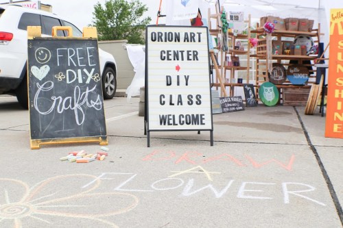 A chalkboard sign for free DIY crafts and a welcome sign for a DIY class at the Orion Art Center, with chalk drawings on the ground.
