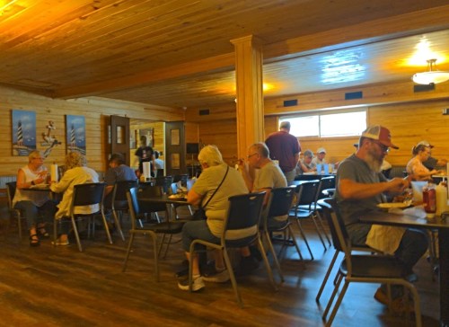 A cozy restaurant interior with diners at tables, wooden walls, and a warm atmosphere.