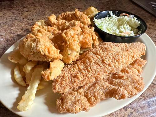 A plate of fried chicken, fish fillets, crinkle-cut fries, and a side of coleslaw.
