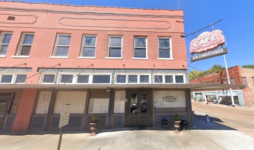 Historic pink building with large windows, featuring a sign for a café and a small outdoor seating area.