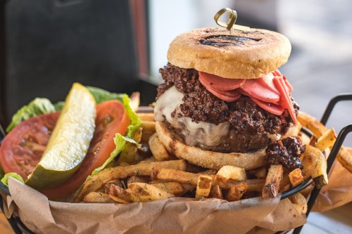 A juicy burger with melted cheese, pickled onions, and a side of crispy fries, garnished with lettuce, tomato, and pickles.