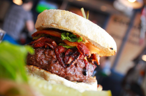 Close-up of a juicy burger with bacon, lettuce, and tomato, served on a toasted bun.