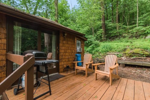 Cozy cabin deck with two chairs, a grill, and lush green forest surroundings.