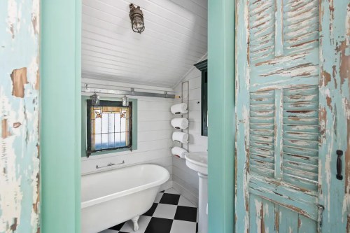 A vintage-style bathroom featuring a freestanding tub, checkered floor, and teal accents with stained glass windows.