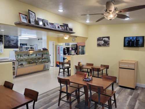 Cozy café interior with yellow walls, wooden tables, a display case, and a TV, creating a welcoming atmosphere.