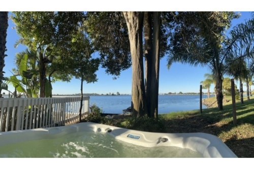 A hot tub beside a serene lake, surrounded by trees and clear blue skies.