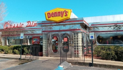 A shiny, retro-style Denny's diner with a bright yellow sign and classic chrome exterior on a clear day.