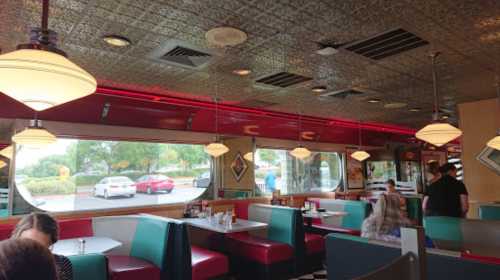 Interior of a retro diner with colorful booths, pendant lights, and large windows showing cars outside.