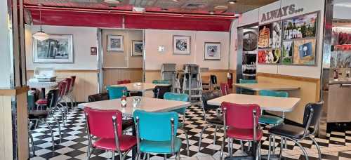 A retro diner interior with colorful chairs, checkered floor, and tables, featuring framed artwork on the walls.